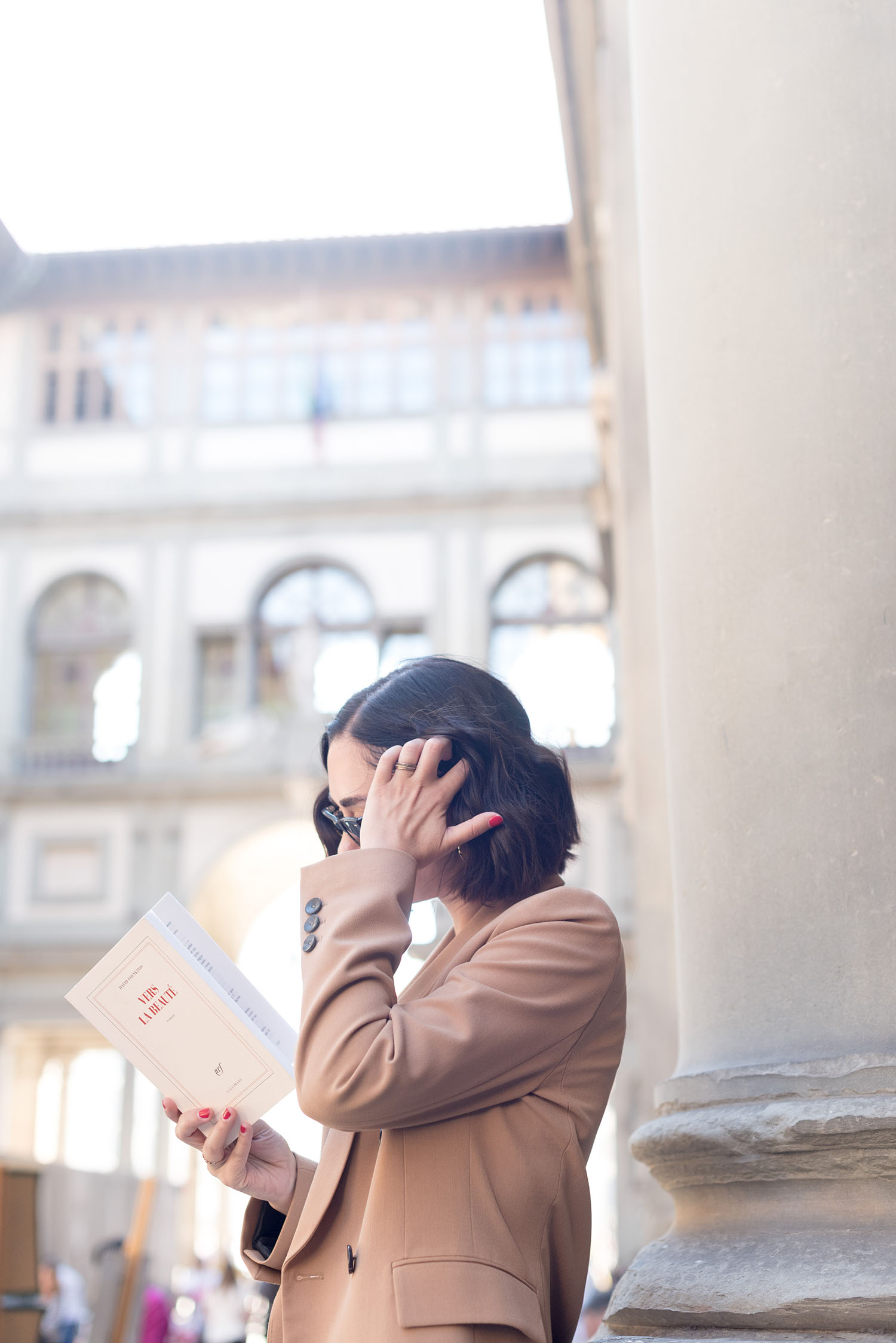 Top Canadian fashion blogger Cee Fardoe of Coco & Vera stands outside the Uffizi Gallery reading, wearing a Zara camel blazer and Madewell rings