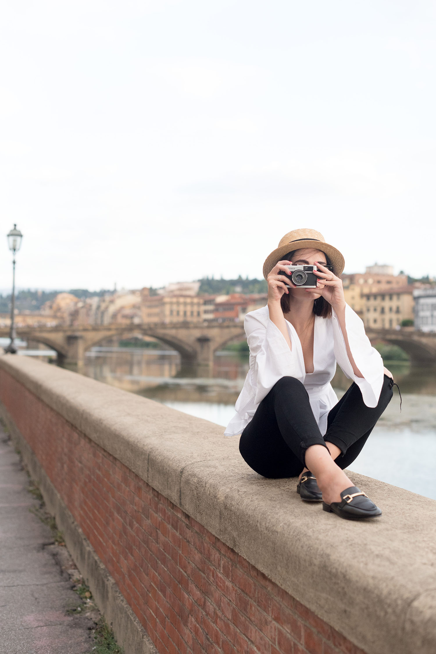 Best Winnipeg fashion blogger Cee Fardoe of Coco & Vera sits near the Arno river in Florence, wearing Jonak mules and Paige jeans